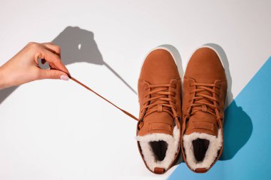 Beyaz ve mavi arka planda Unisex kahverengi kış ayakkabıları. Kadın eli ayakkabıları dantelden çeker, yakın plan, düz yatar.