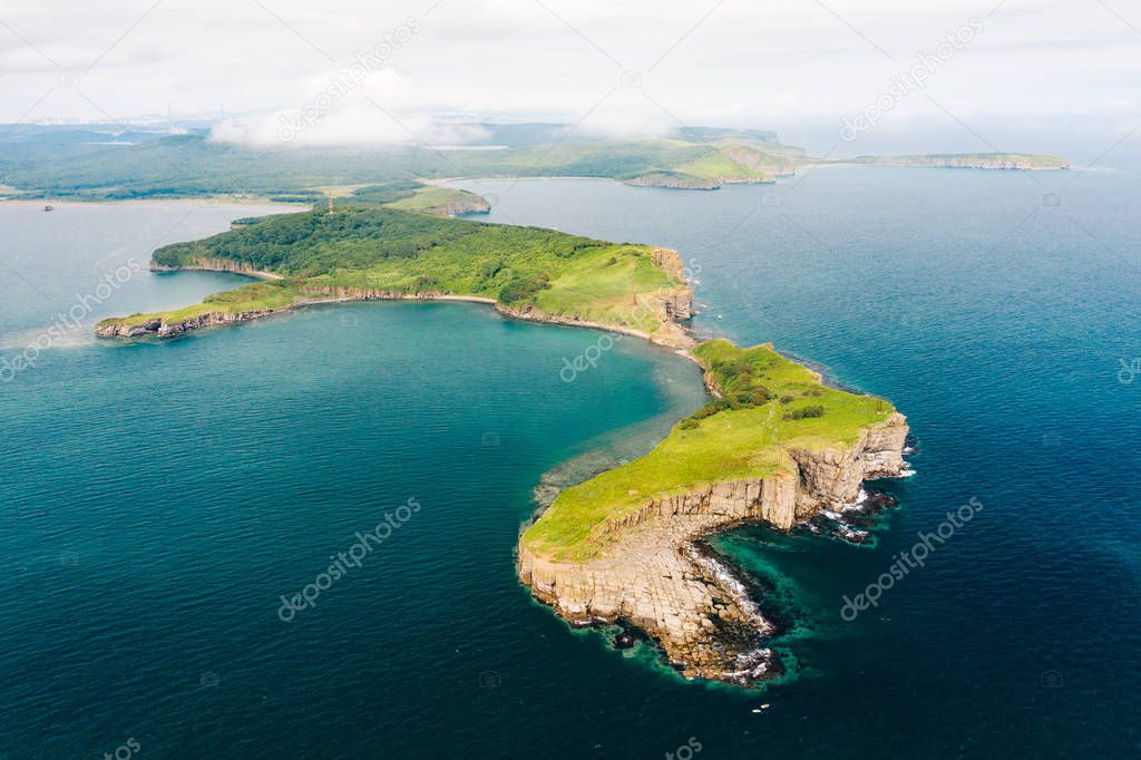 Aerial view of Cape Tobizina, Russky Island near Vladivostok. Green forest at blue sea coast, rocky and steep cliffs, sunny summer day. Seaside nature landscape in Primorsky Krai, Far East, Russia