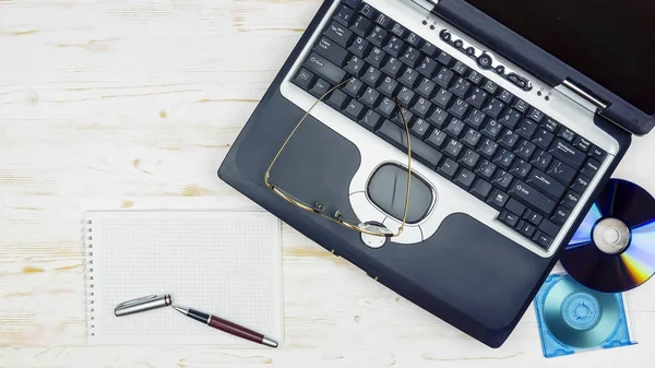 old laptop with floppy disks, a notebook, glasses and a pen