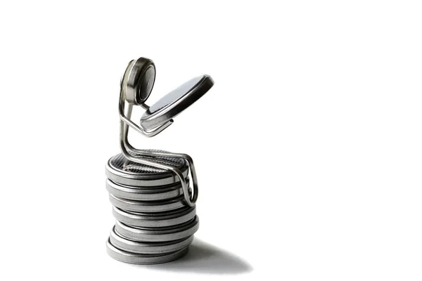 A paper clip in the form of a man with a face made of a round battery sits on a column of batteries. In the hands of a man holding a round battery. Macro mode. Copy space.