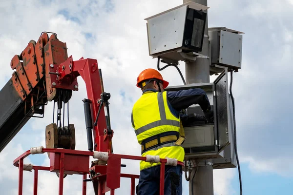 The operator repairs the video recording camera of traffic violations. The camera is attached to the lighting mast. The operator stands in the cradle of the truck crane for lifting people.