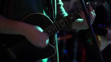 Erkek müzisyen bir penayla akustik gitar çalıyor, yakın plan, gece kulübü / konser salonunda çekim yapıyor, yavaş çekim.
