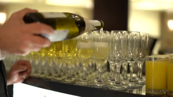 Na stole je velké množství sklenic, barman / číšník v bílé košili do nich nalije šampaňské, zpomalené, umělé osvětlení