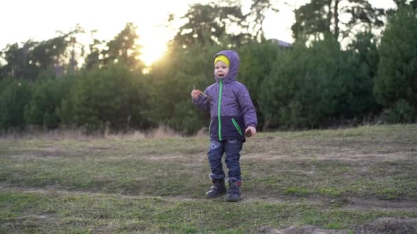 一个孩子站在小径上 穿着一件秋装 牛仔裤和一双暖和的靴子 在背景下 你可以看到树木和夕阳 孩子正在标志着时间的流逝 大声喊着 — 图库视频影像