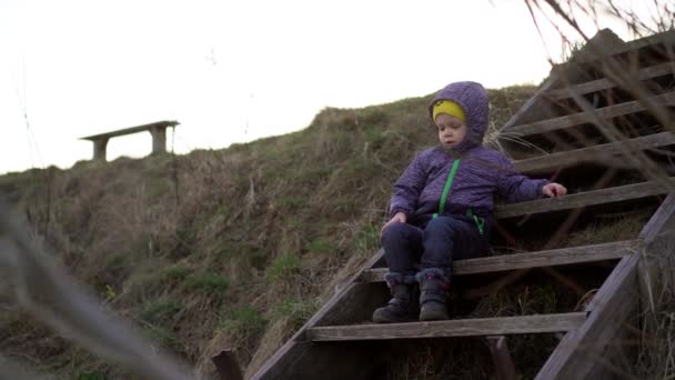 Mały Chłopiec Półsezonowej Kurtce Dżinsach Siedzi Wieczorem Drewnianych Schodach Zboczu — Wideo stockowe