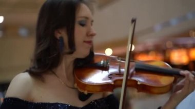 Kahverengi saçlı bir kadın, mavi gece elbisesi ve pulları olan, keman çalan, yandan çekim yapan, yavaş çekim yapan