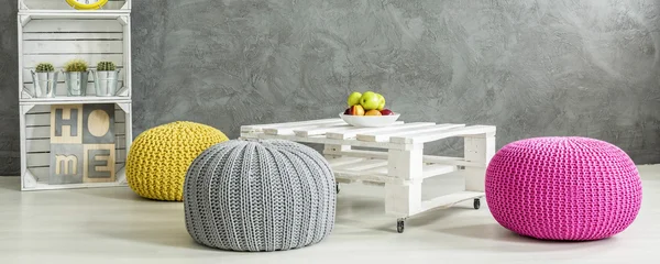 Quarto cinzento com uma mesa rodeada por pufes coloridos — Fotografia de Stock