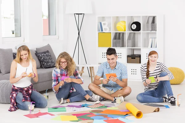 Friends sitting on the floor and making a paper cutouts — Stockfoto