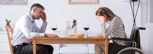 Homem sentado à mesa na frente de sua esposa em uma cadeira de rodas — Fotografia de Stock