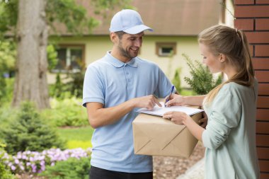 Courier holding a parcel and woman signing a delivery form