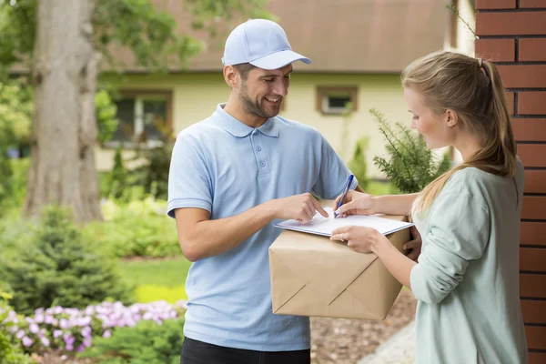 Courier holding a parcel and woman signing a delivery form — Stock Photo, Image