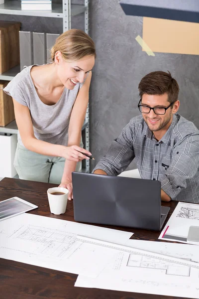 Woman is standing next to her co-worker who is working on his laptop — Stock Photo, Image