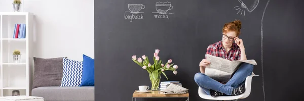 Young girl reading newspaper in a modern cafe — Stock Photo, Image