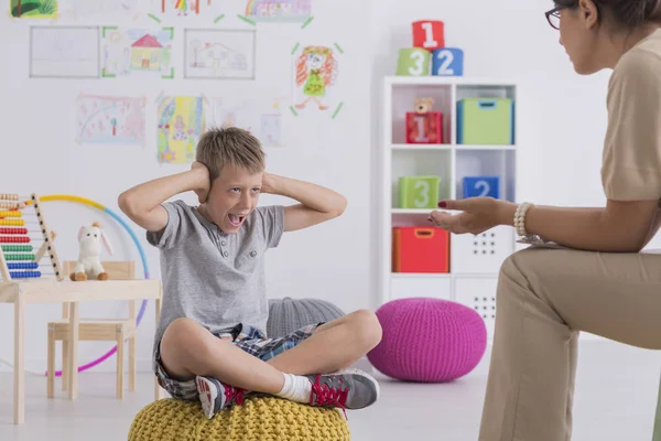 Niño grosero sentado en un puf, cubriéndose las orejas — Foto de Stock