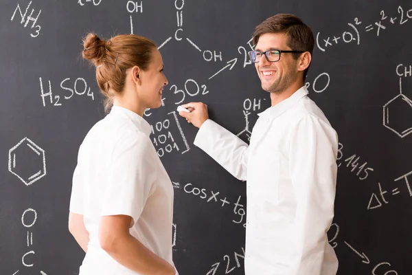 Man and woman wearing labcoats standing in front of a blackboard — Stock Photo, Image