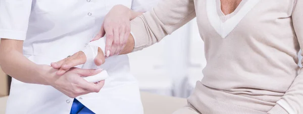 Doctor bandaging senior lady's hand — Stock Photo, Image