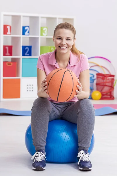 Egzersiz topu üzerinde oturan ve basketbol tutan kadın
