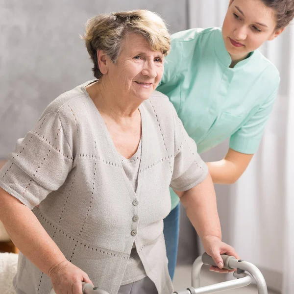 Äldre kvinna med rullator och vårdare — Stockfoto