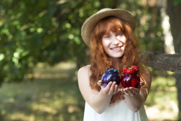 Girl holding jars of strawberries and blueberries — Stock Photo, Image
