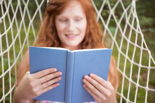 Usmívající se žena čte v houpací síti — Stock fotografie