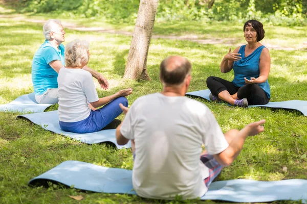 Seniors sitting on exercise mats in a park — Stock Photo, Image