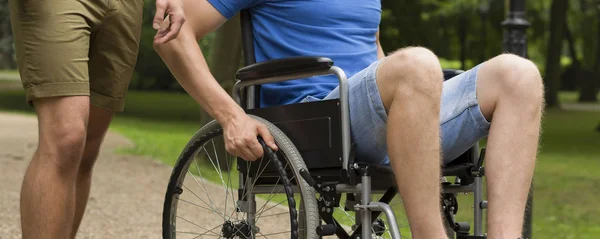 Człowiek na wózku inwalidzkim z przyjacielem w parku — Zdjęcie stockowe