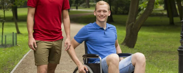 Homem sorridente em uma cadeira de rodas com outro homem — Fotografia de Stock