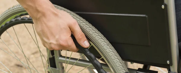 Main d'homme appuyée sur le volant du fauteuil roulant — Photo