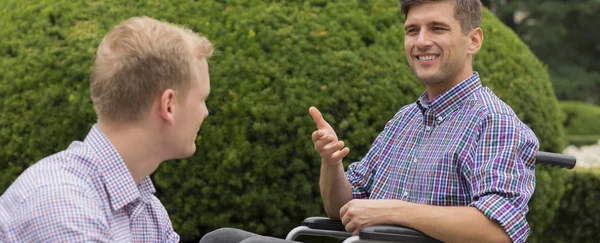 Młody człowiek na wózku inwalidzkim z przyjacielem — Zdjęcie stockowe
