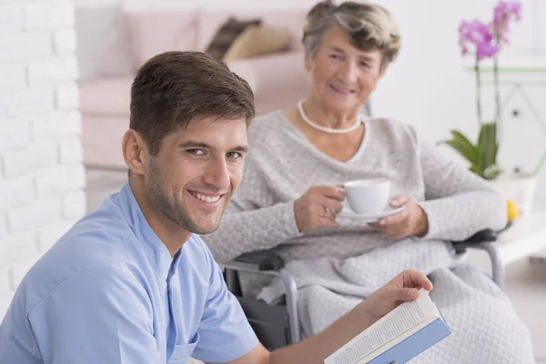 Pflegerin liest Seniorin mit Tee vor — Stockfoto
