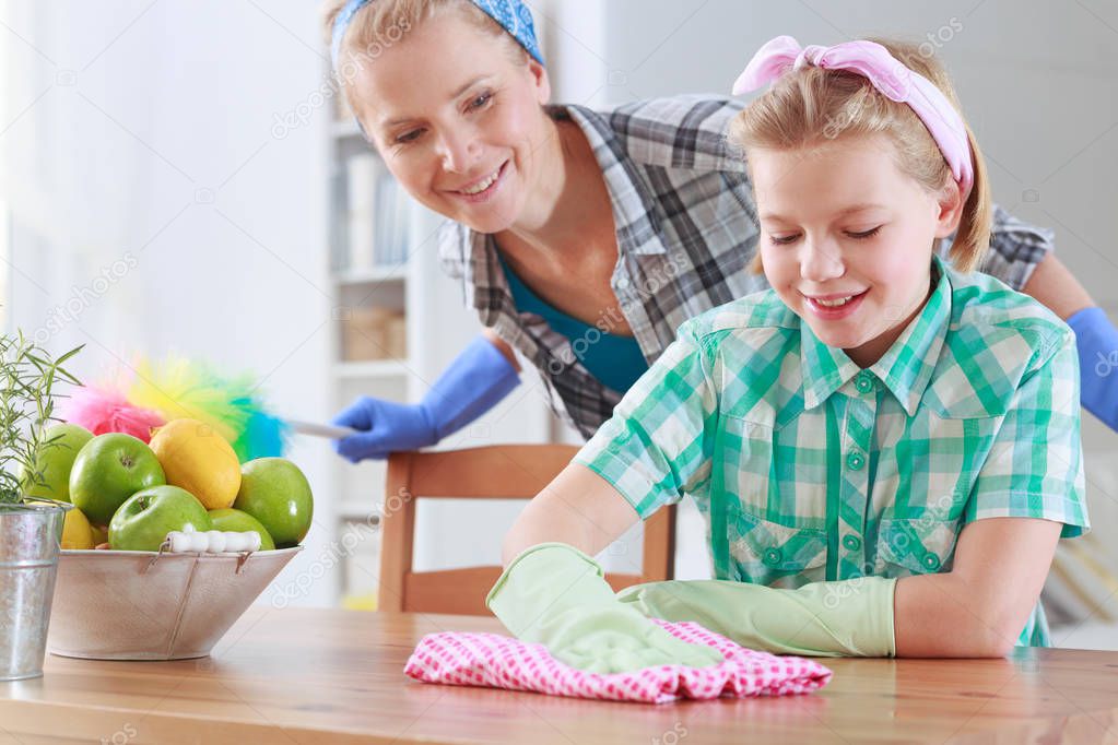 Girl wiping a table and her mum watching her