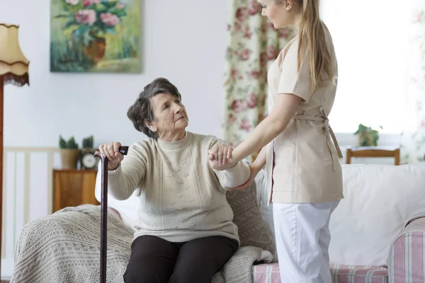 Enfermeira ajudando a mulher idosa a se levantar — Fotografia de Stock