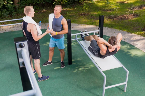 Hombre haciendo abdominales y sus amigos descansando —  Fotos de Stock