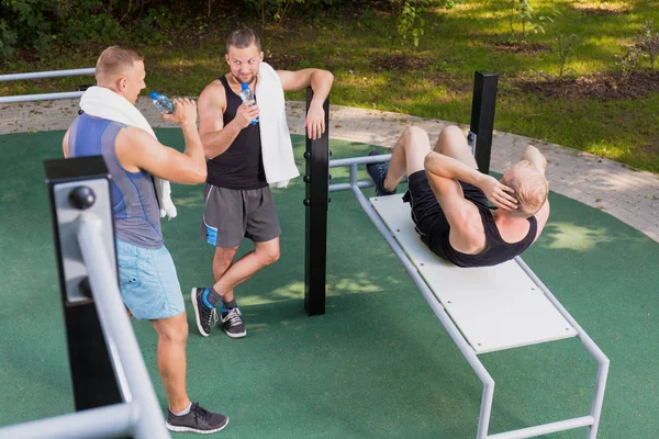 Mann macht Sit-ups und seine Freunde trinken Wasser — Stockfoto