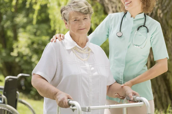 Пожилая женщина с медсестрой, помогающей ей — стоковое фото