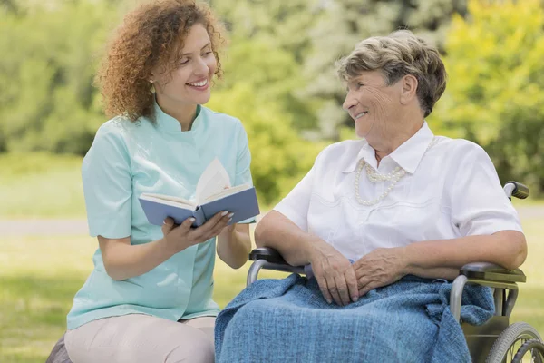 Sjuksköterska läsa äldre kvinna i en trädgård — Stockfoto