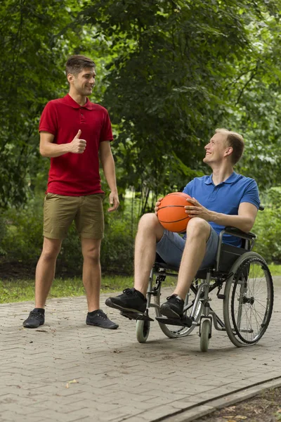 Man with friend on wheelchair holding a basketball — Stock Photo, Image