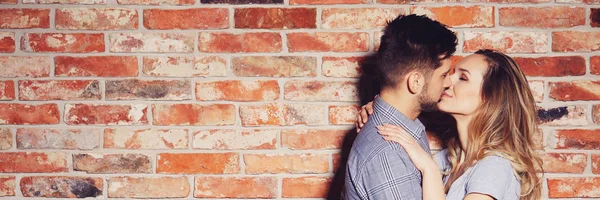 Couple kissing against brick wall — Stock Photo, Image