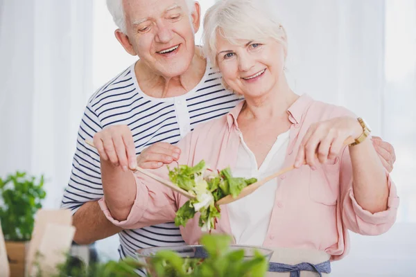 Äldre kvinna och man förbereder sallad — Stockfoto
