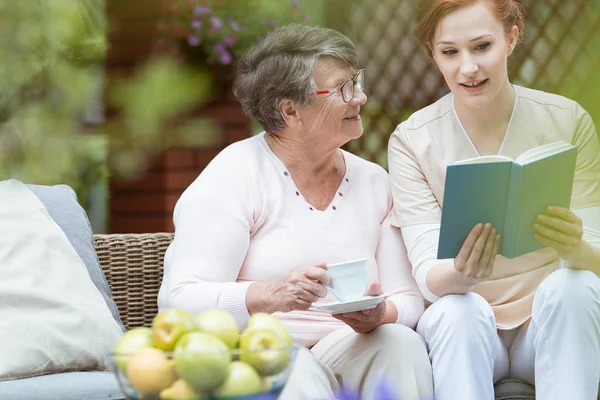 Nurse reading to pensioner — Stock Photo, Image