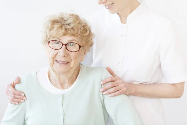 Lachende assistent knuffelen oude dame — Stockfoto