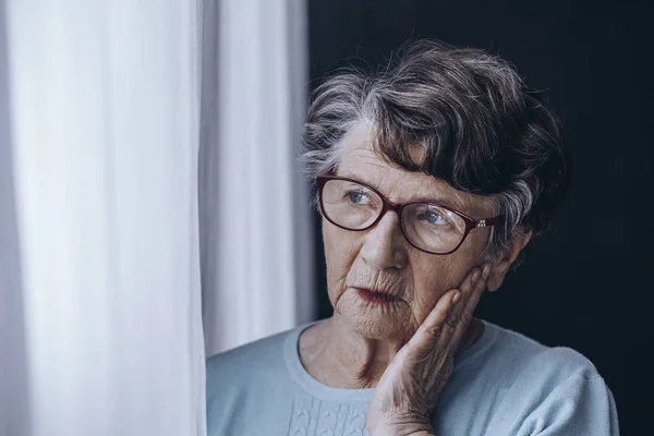 Elderly woman looking through window — Stock Photo, Image