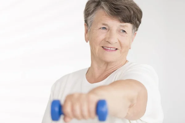 Elderly woman holding blue dumbbell — Stock Photo, Image