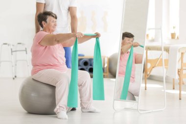 Elderly woman exercising shoulders muscles clipart