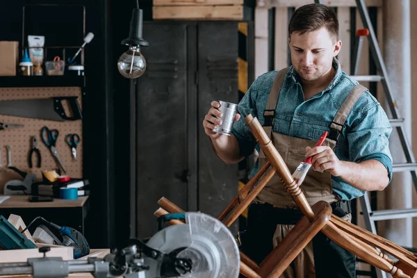 Улыбающийся плотник ремонтирует деревянное кресло — стоковое фото
