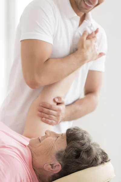 Physiotherapist stretching senior woman's shoulder — Stock Photo, Image