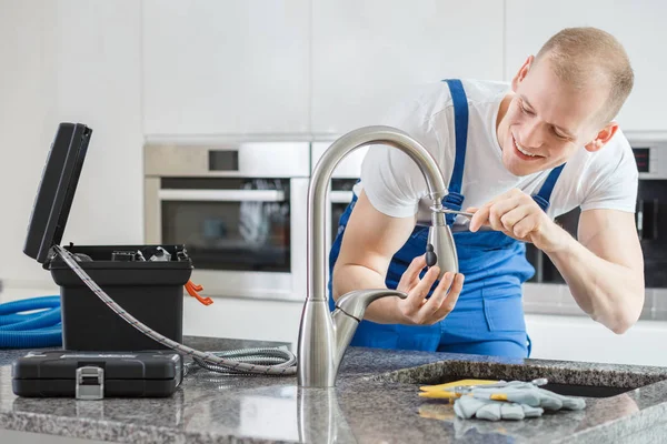 Happy plumber repairing kitchen's faucet — Stock Photo, Image