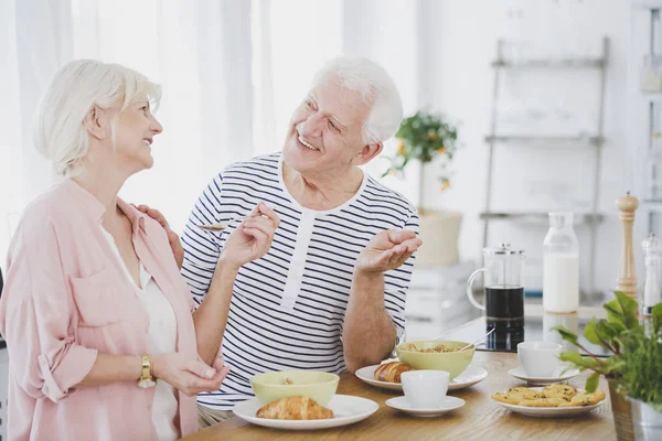 Lachende senior paar eten croissants — Stockfoto