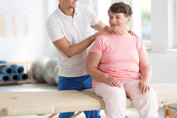 Fisioterapeuta masajeando sonriente mujer mayor —  Fotos de Stock