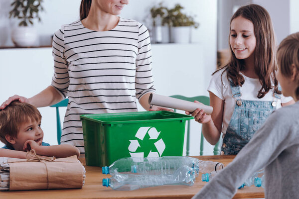 Aware mother teaching smiling children how to recycle household waste